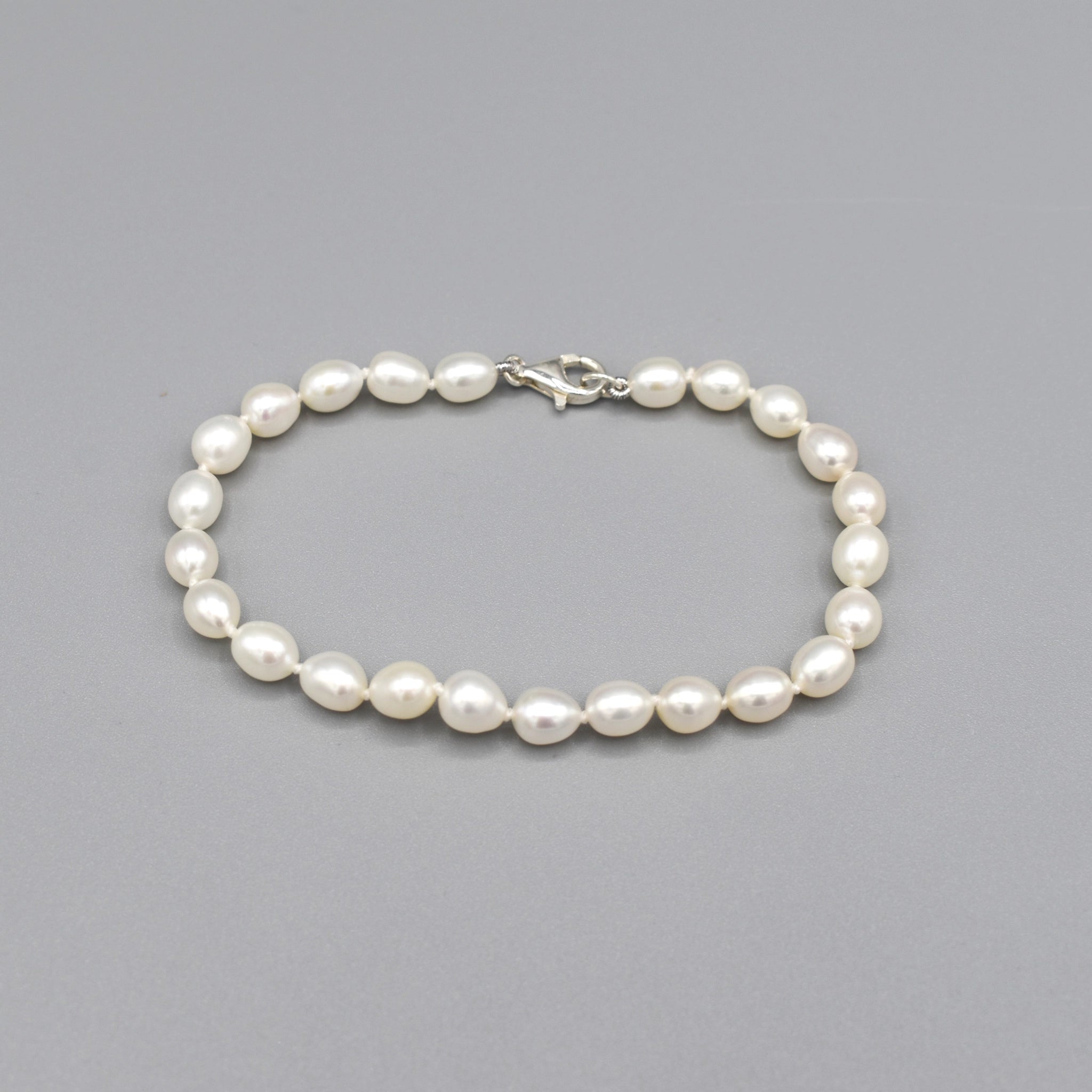 A silver lobster clasp bracelet strung with small oval shaped white freshwater pearls