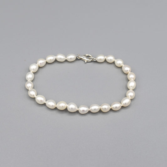 A silver lobster clasp bracelet strung with small oval shaped white freshwater pearls