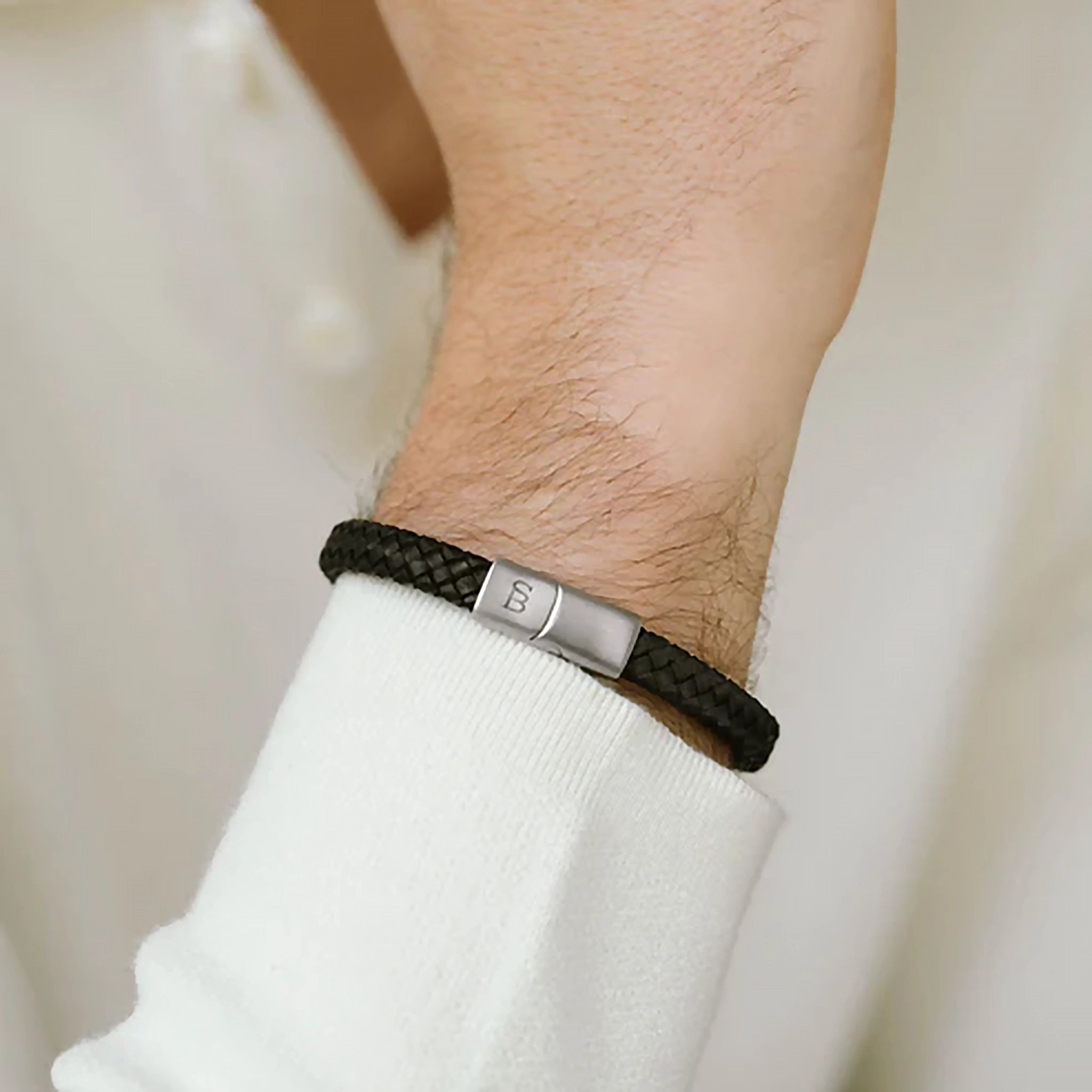 Model wearing a braided band black leather bracelet with monogramed stainless steel clasp