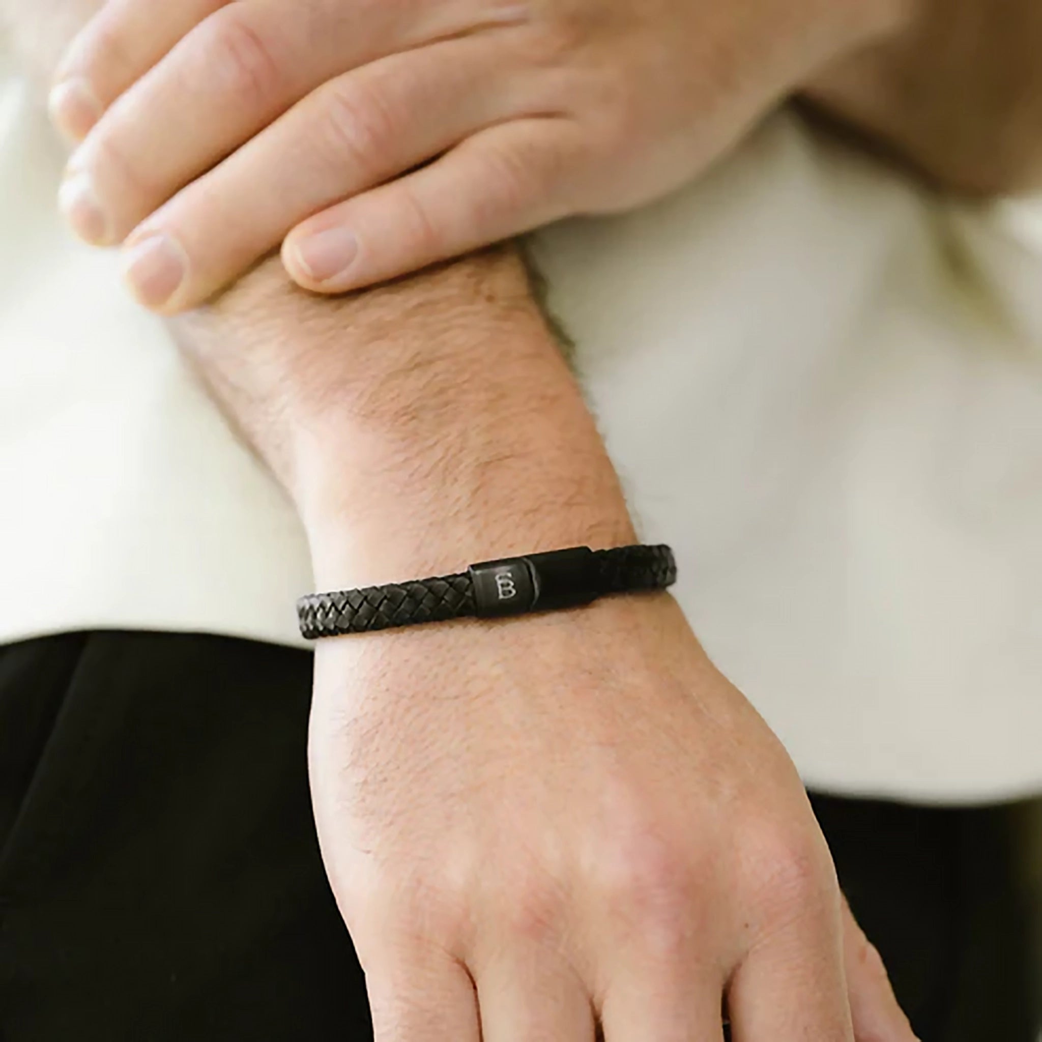 Model wearing a braided band black leather bracelet with monogramed black stainless steel clasp