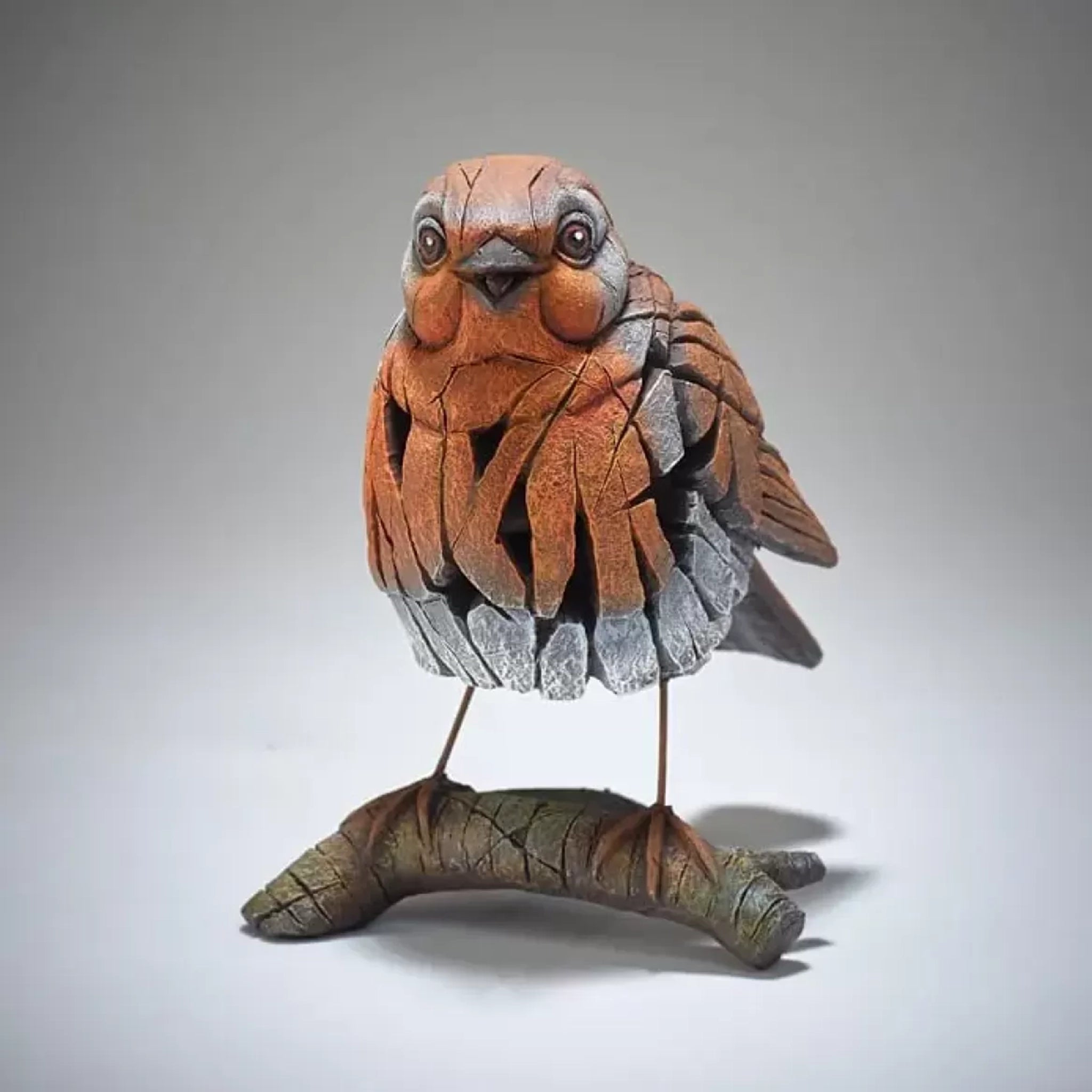 A textured and painted robin on a branch figure sculpture front view