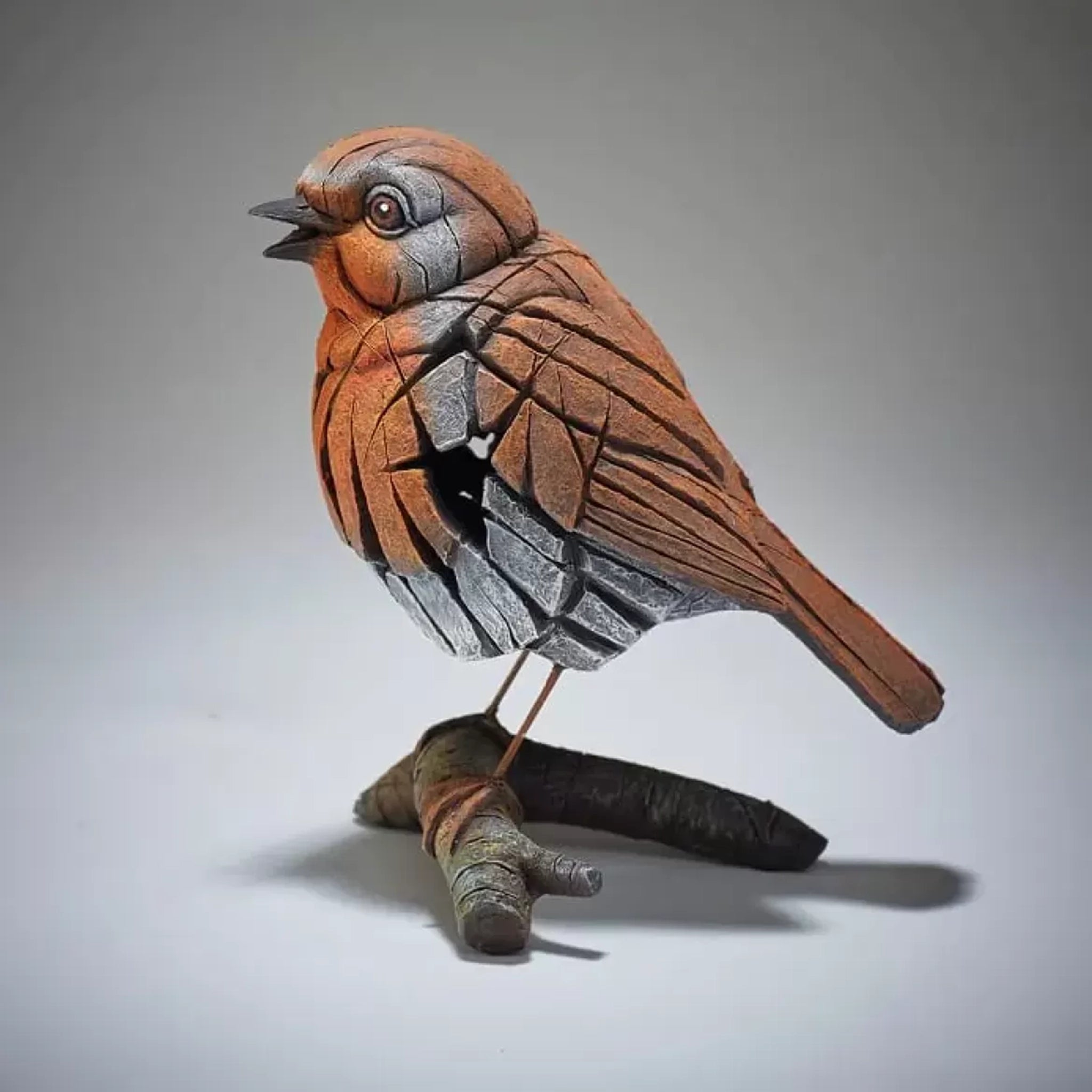 A textured and painted robin on a branch figure sculpture side view