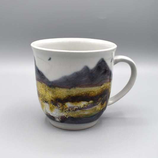 A large pottery mug featuring a hand painted pattern of a rocky landscape