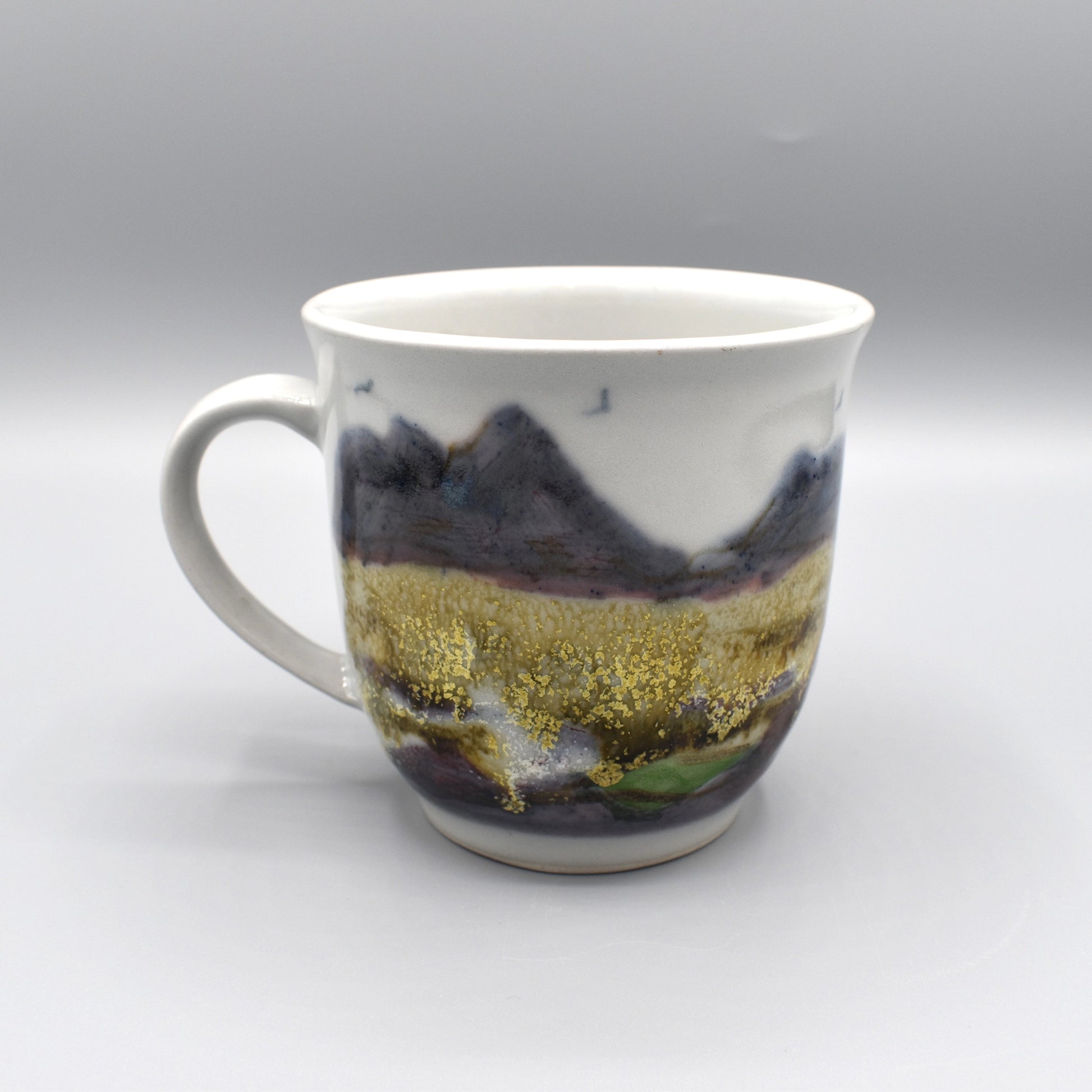 A large pottery mug featuring a hand painted pattern of a rocky landscape