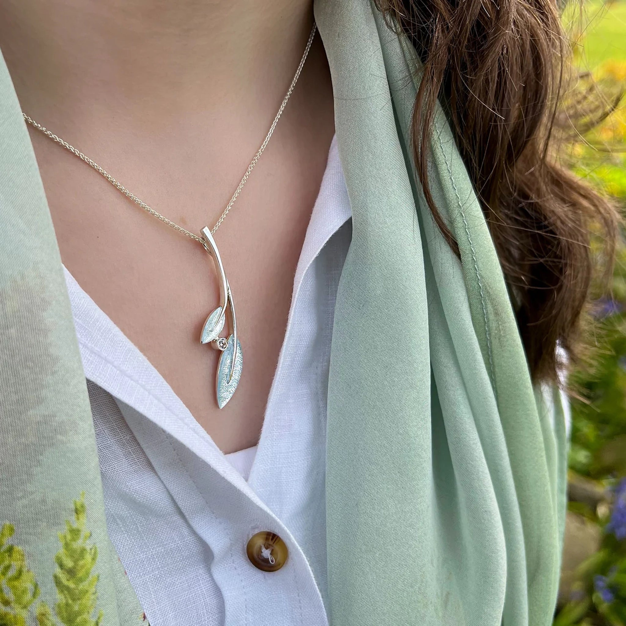 Model wearing silver pendant with double rowan tree leaves, a frosty white enamel and cubic zirconia, on a silver chain