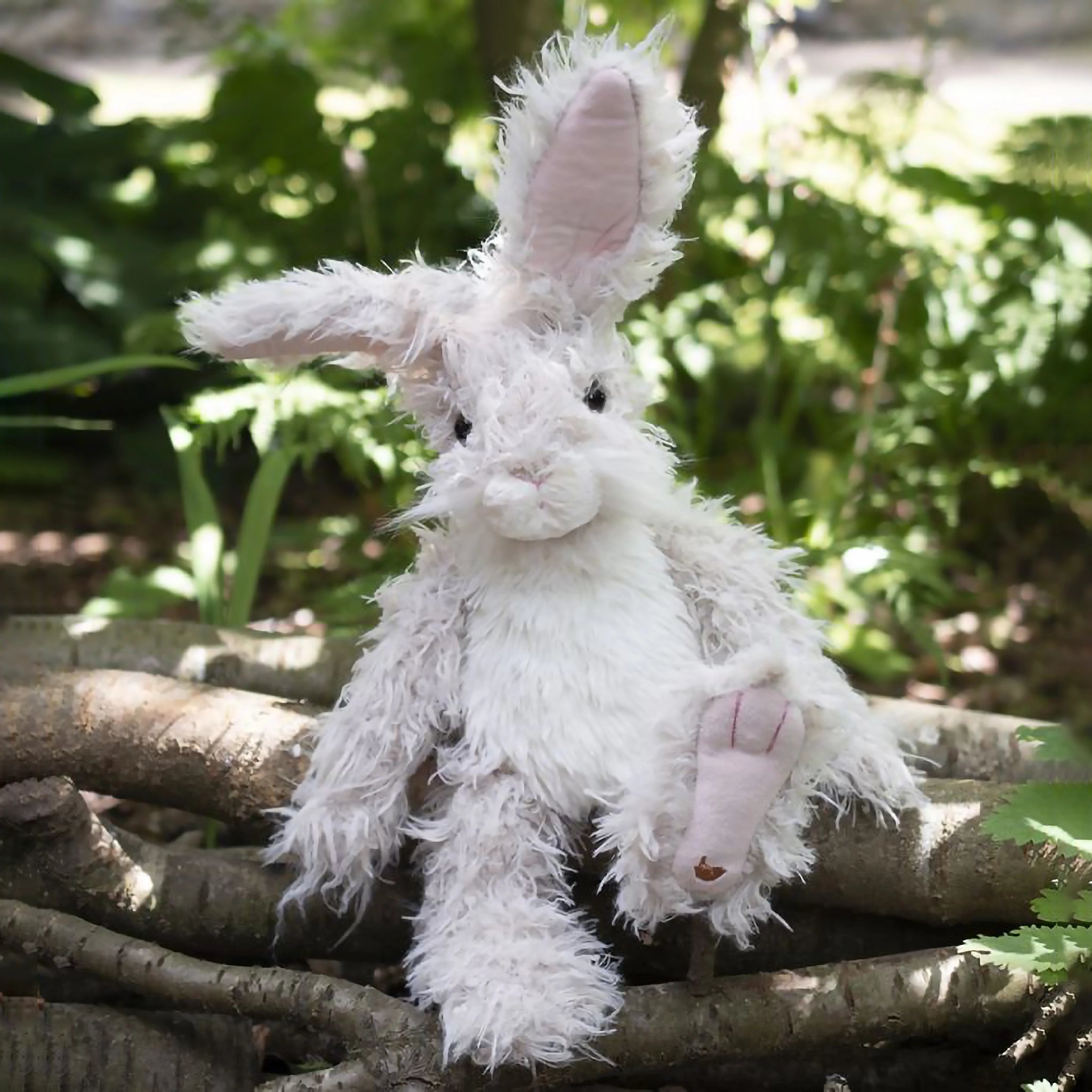 A stuffed hare plush toy with the Wrendale logo embroidered on the bottom of its foot posed on branches