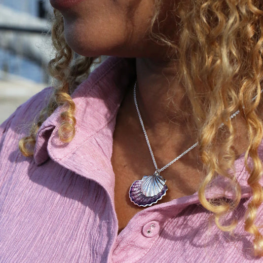 Model wearing a silver pendant in the shape of a scallop shell with pink enamelling and a chunky chain