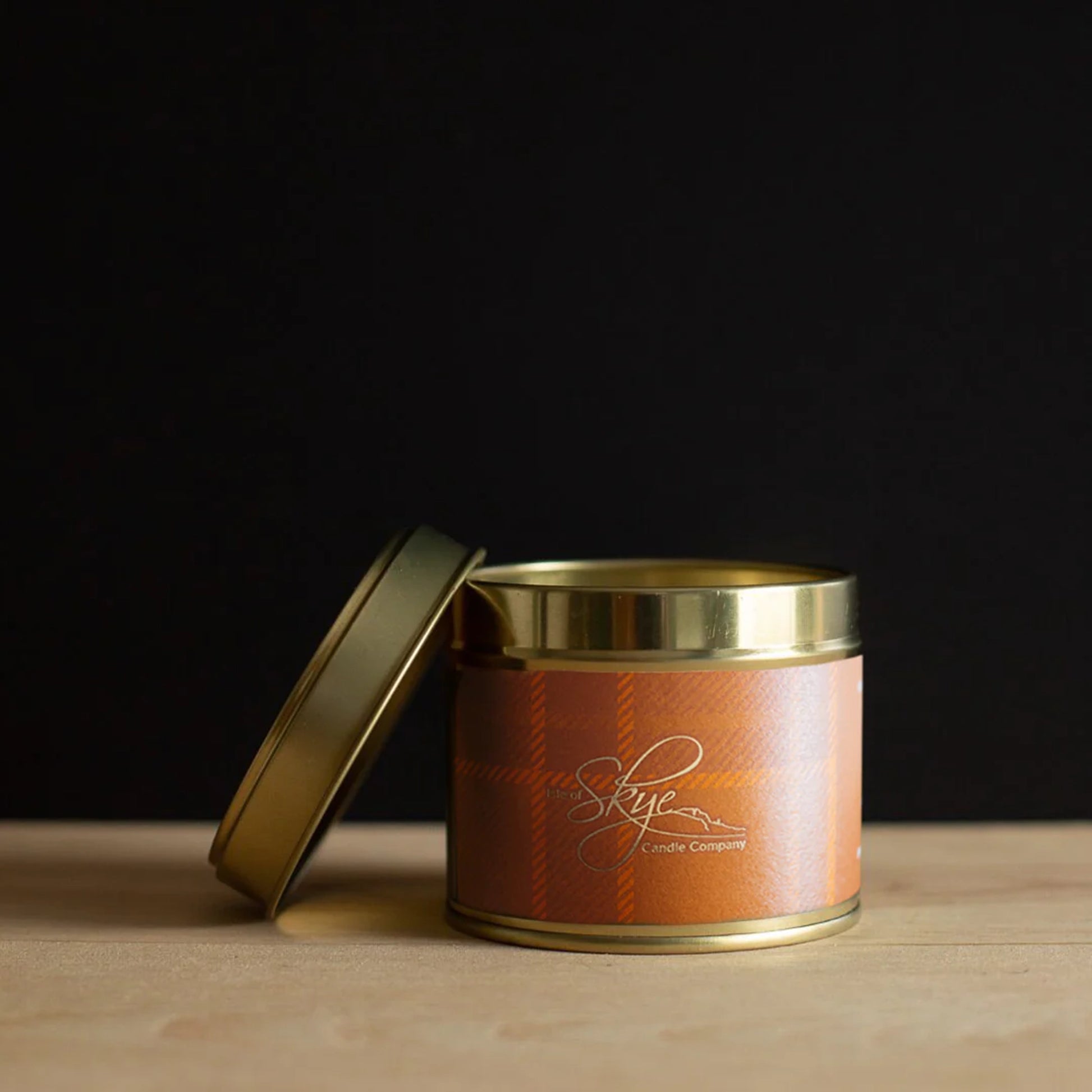 Gold toned travel tin candle with orange tartan design in the scent Island whisky