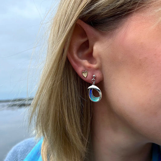 Model wearing silver drop earrings with bright blue enamel in a simple abstract ocean wave shape on a drop post fittings