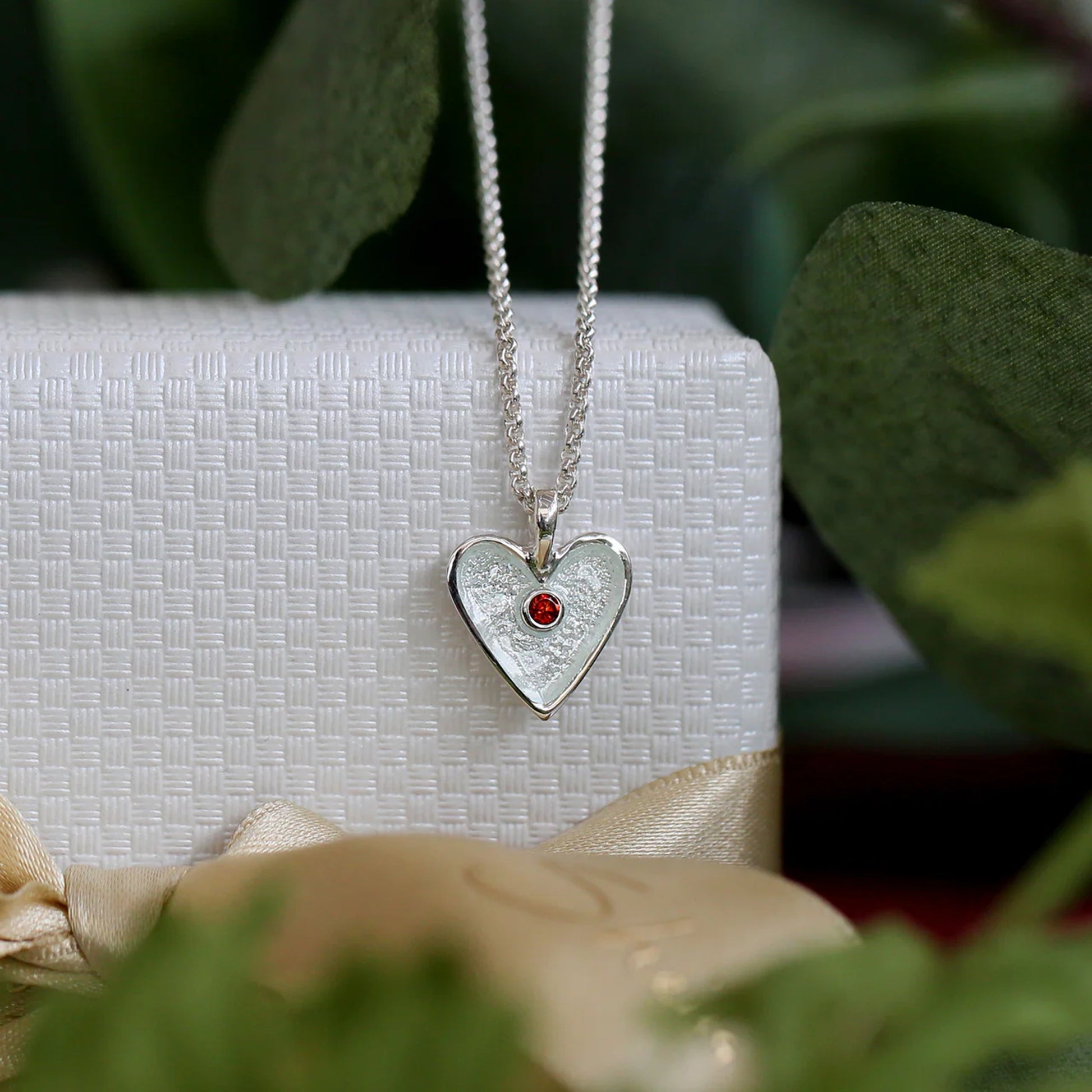 Heart shaped silver pendant in white enamel with a red garnet stone in the centre and a silver chain lifestyle