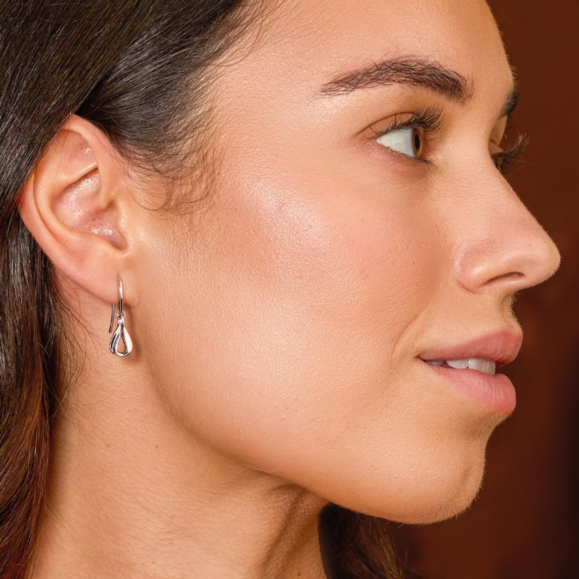 Model wearing a pair of silver ribbon twist loop drop earrings