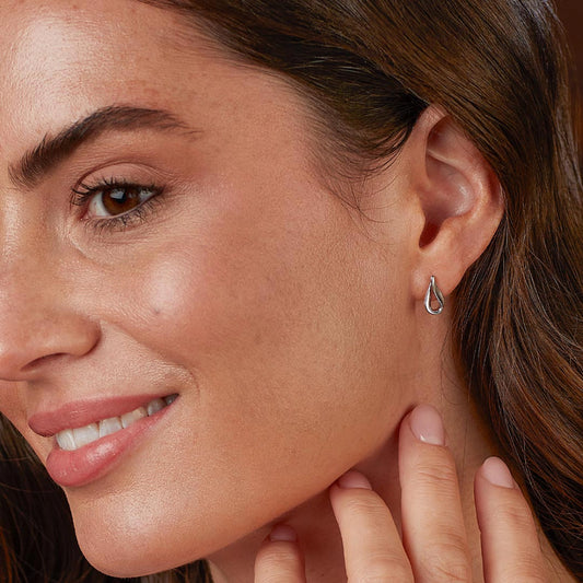 Model wearing a pair of small silver twist stud earrings in a soft ribbon-like shape