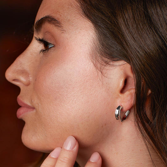 Model wearing a pair of silver huggie hoop earrings with a ribbon like shape