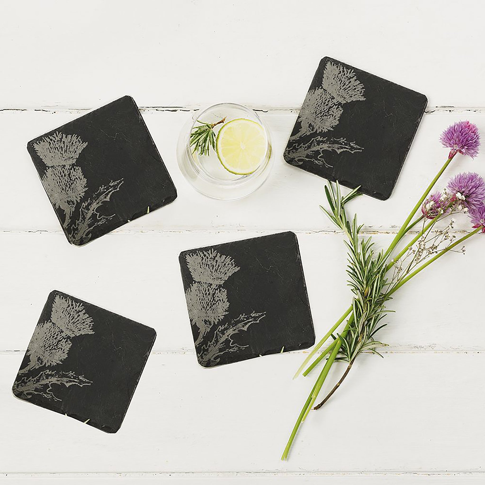 4 square slate coasters engraved with a Scottish thistle on each staged on a table