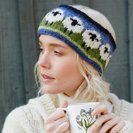Model wearing a knitted headband in green and blue with a row of white sheep