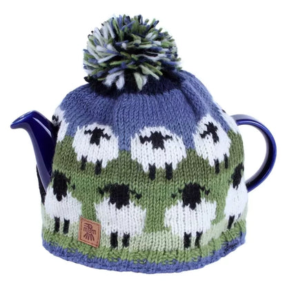 A knitted tea cosy featuring sheep in field in green and blue on a teapot