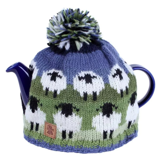 A knitted tea cosy featuring sheep in field in green and blue on a teapot