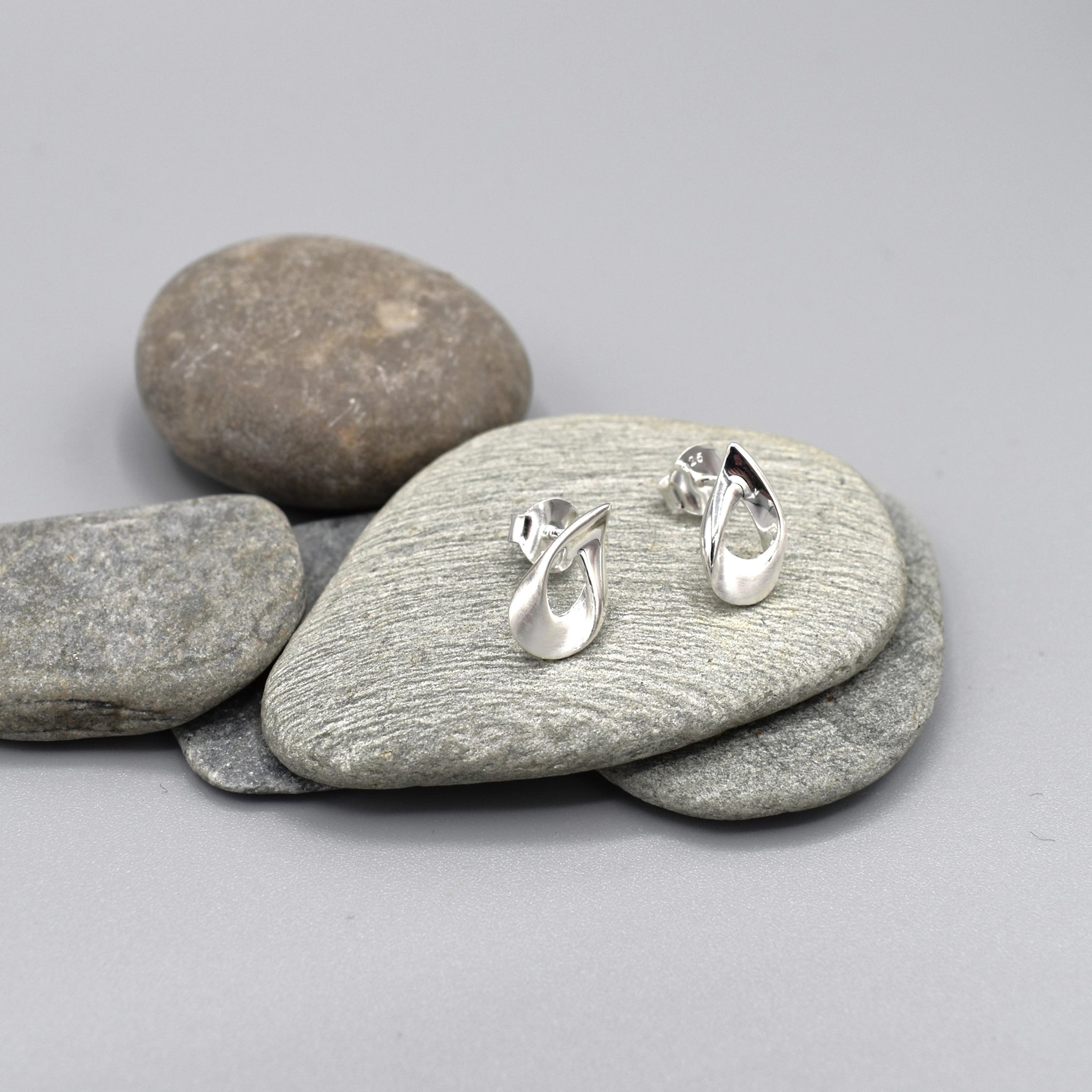 A pair of matt and shiny textured teardrop earrings with a twist at the top