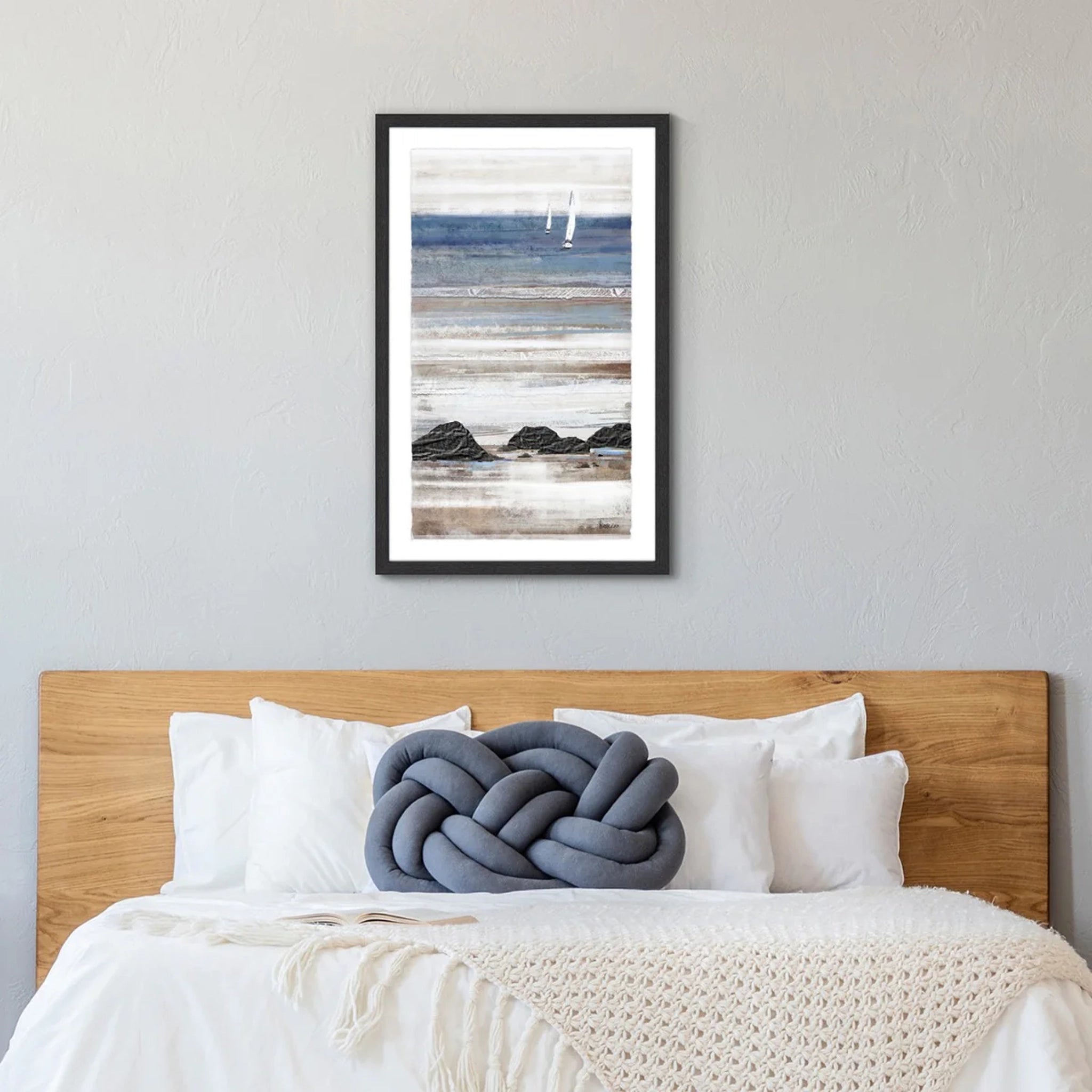 Tall framed print of a seaside with pale blue and sandy colour layers at low tide hanging in a light bedroom.