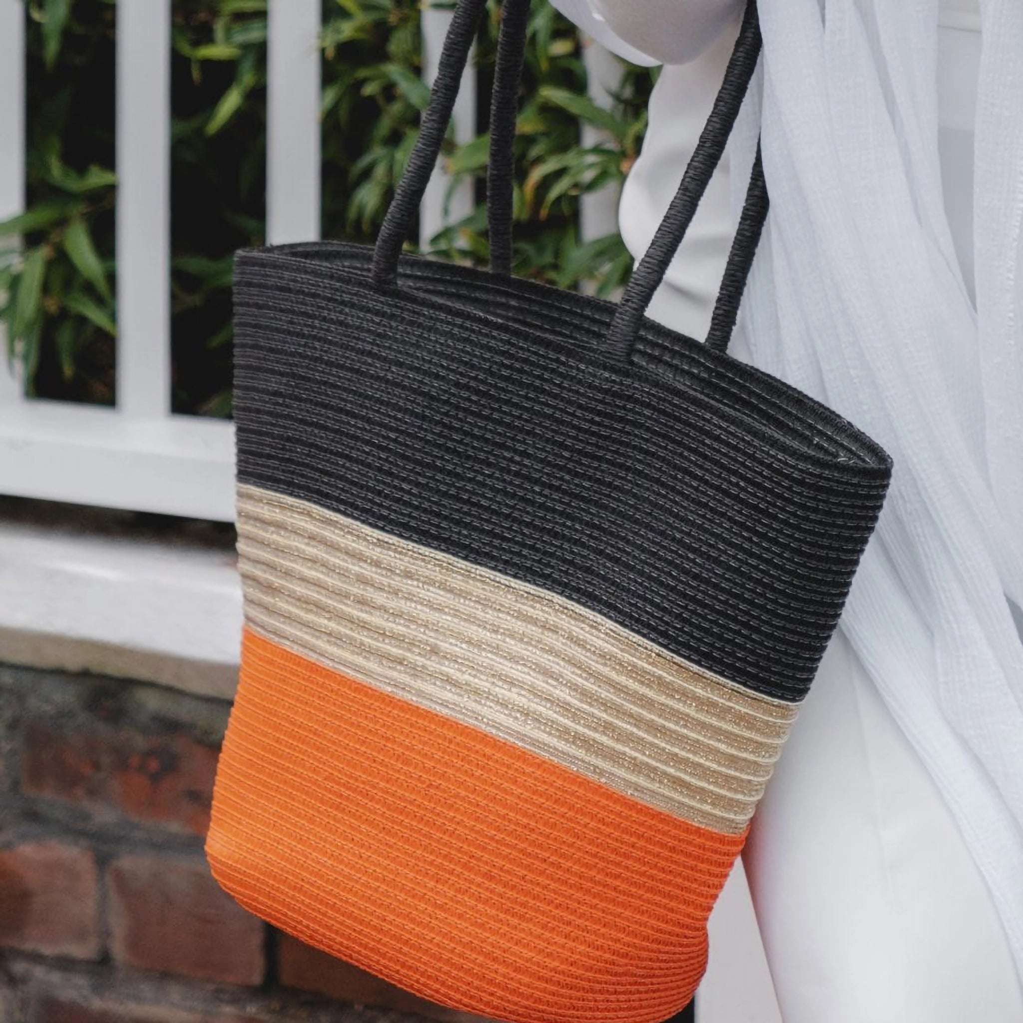 Model holding a woven summer tote bag with black, natural and orange stripes