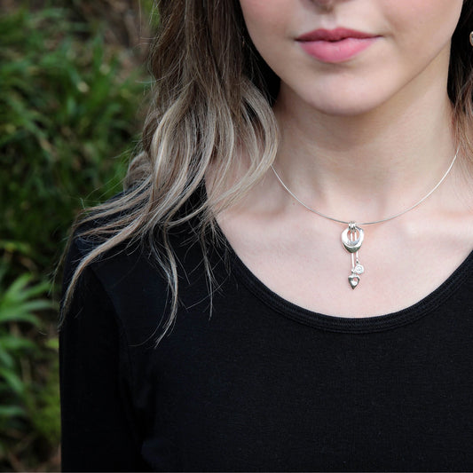 Model wearing a silver necklet featuring an abstract contemporary pendant with swirl and arrow drops