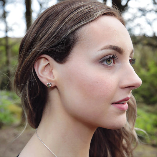 Model wearing a pair of silver abstract heart shaped stud earrings with holes in the centre