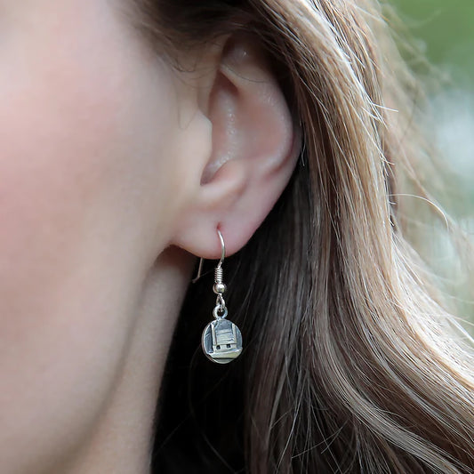 Model wearing a pair of silver drops featuring round coins with raised little cottage houses and textured details