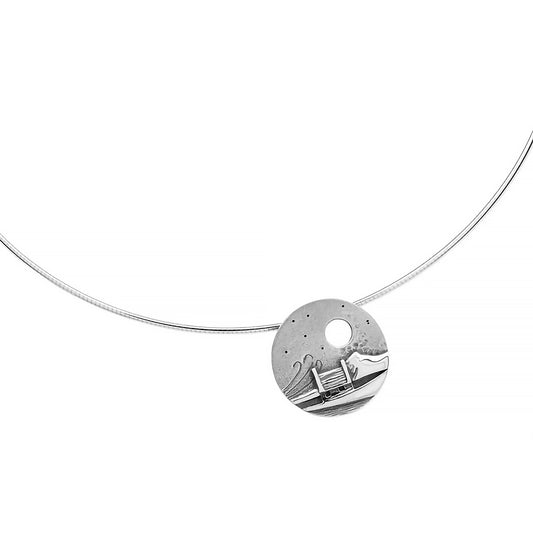 A necklet featuring a round coin pendant with a cottage in a windy scene and cutout moon