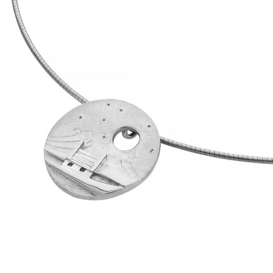 A necklet featuring a round coin pendant with a cottage in a windy scene and cutout moon in detail