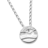 A silver round pendant on a chain featuring a flying sea bird in front of a cutout sun over water