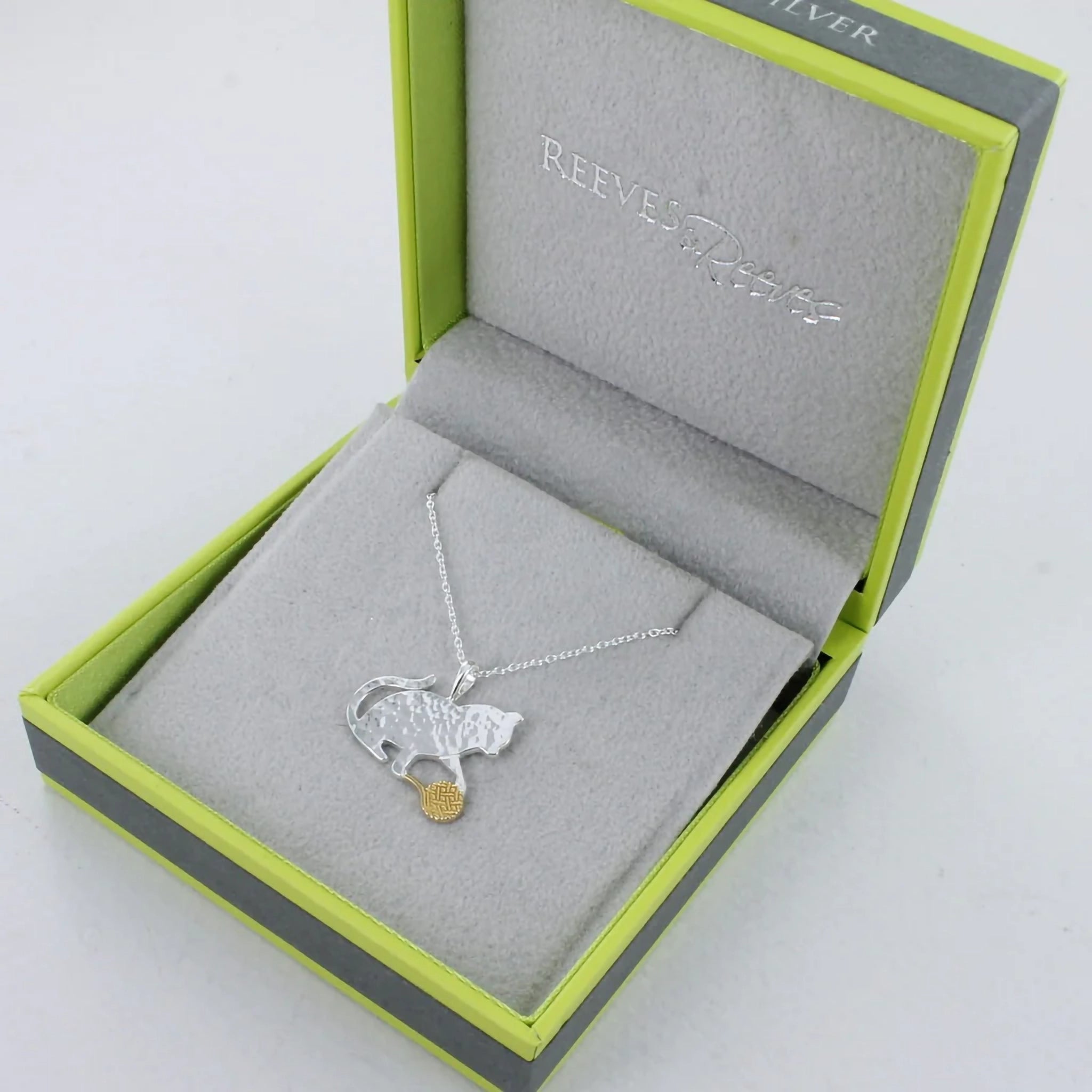 A pendant featuring a silver cat playing with a ball of gold wool in branded box