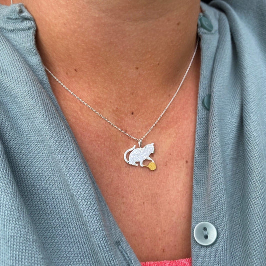 Model wearing a pendant featuring a silver cat playing with a ball of gold wool