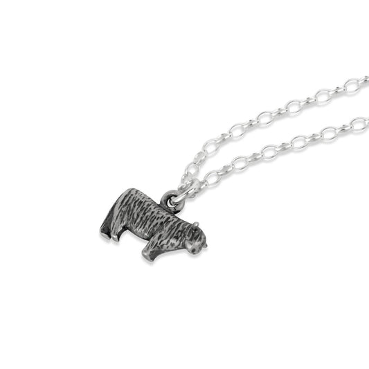 A silver pendant featuring detailed texture, and shaped like a little Highland cow on a silver chain