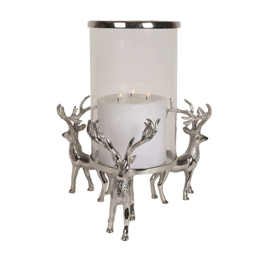A large glass hurricane candle holder with a silver metal base featuring three stags/reindeer