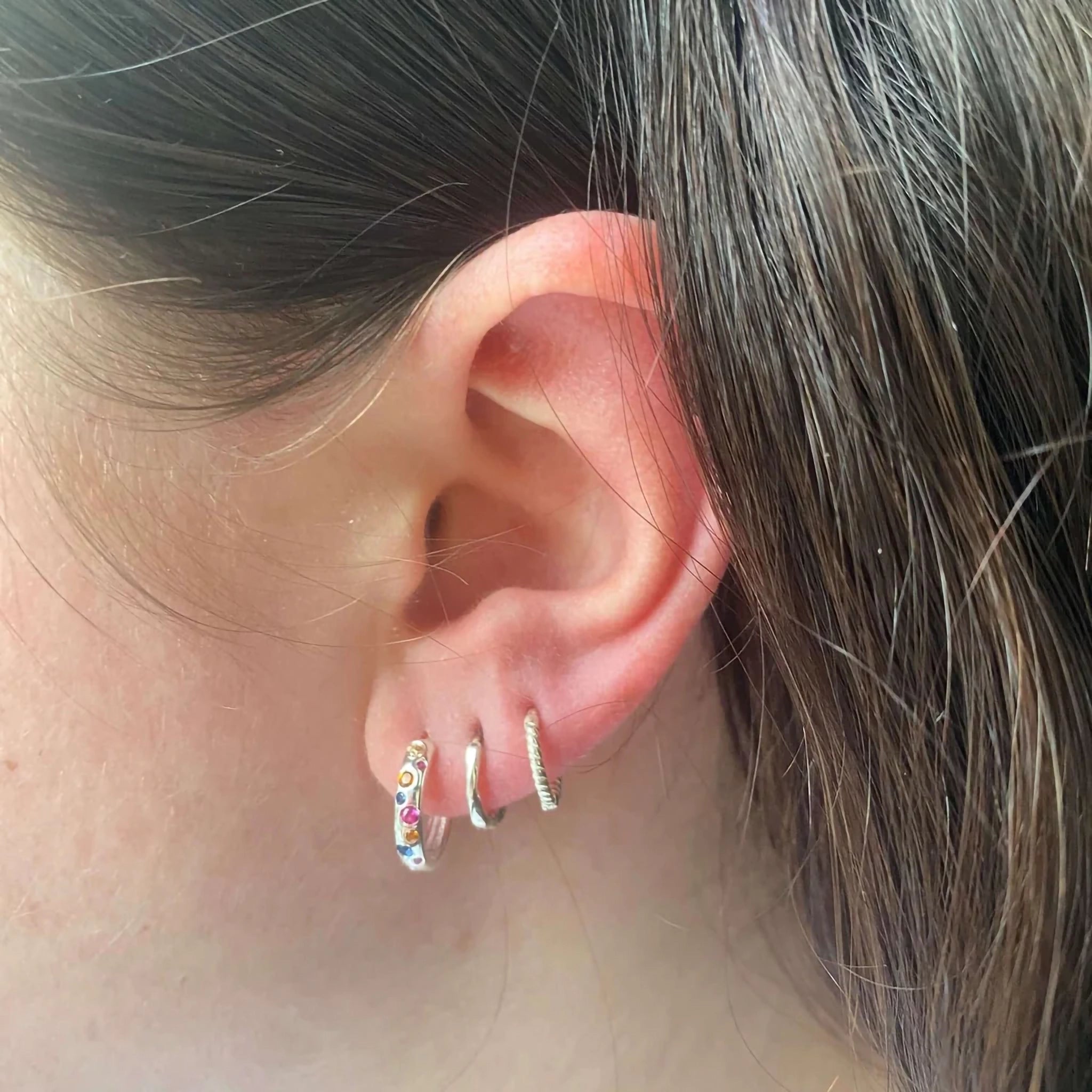 Model wearing a pair of silver hoop earrings with scattered multicoloured stones