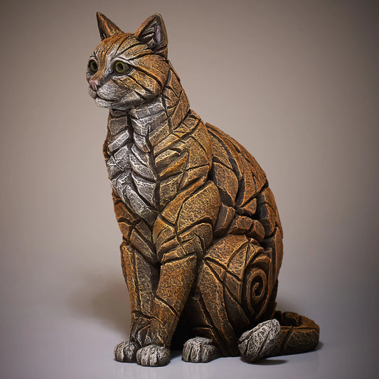 Side view of a modern sculpture of a sitting ginger cat with white chest and toes