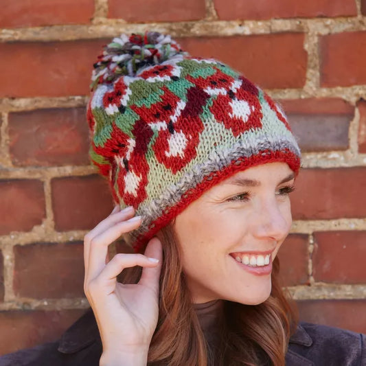 Model wearing a knitted pompom hat in green and orange with rows of foxes