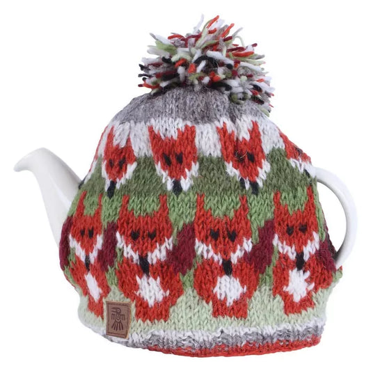 A knitted teacosy with a pompom featuring rows of foxes on a teapot