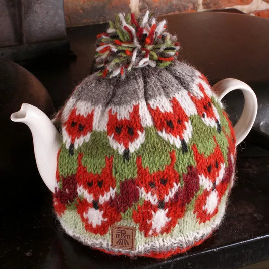 A knitted teacosy with a pompom featuring rows of foxes lifestyle