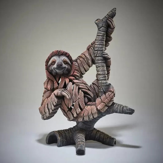 A textured and painted sloth on a branch figure sculpture