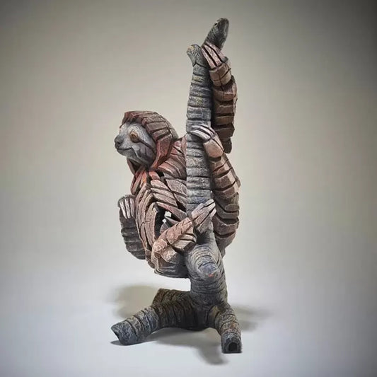 A textured and painted sloth on a branch figure sculpture side view