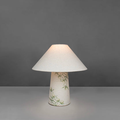 A small fabric table lamp with shade and a thistle design on the conical base lit up
