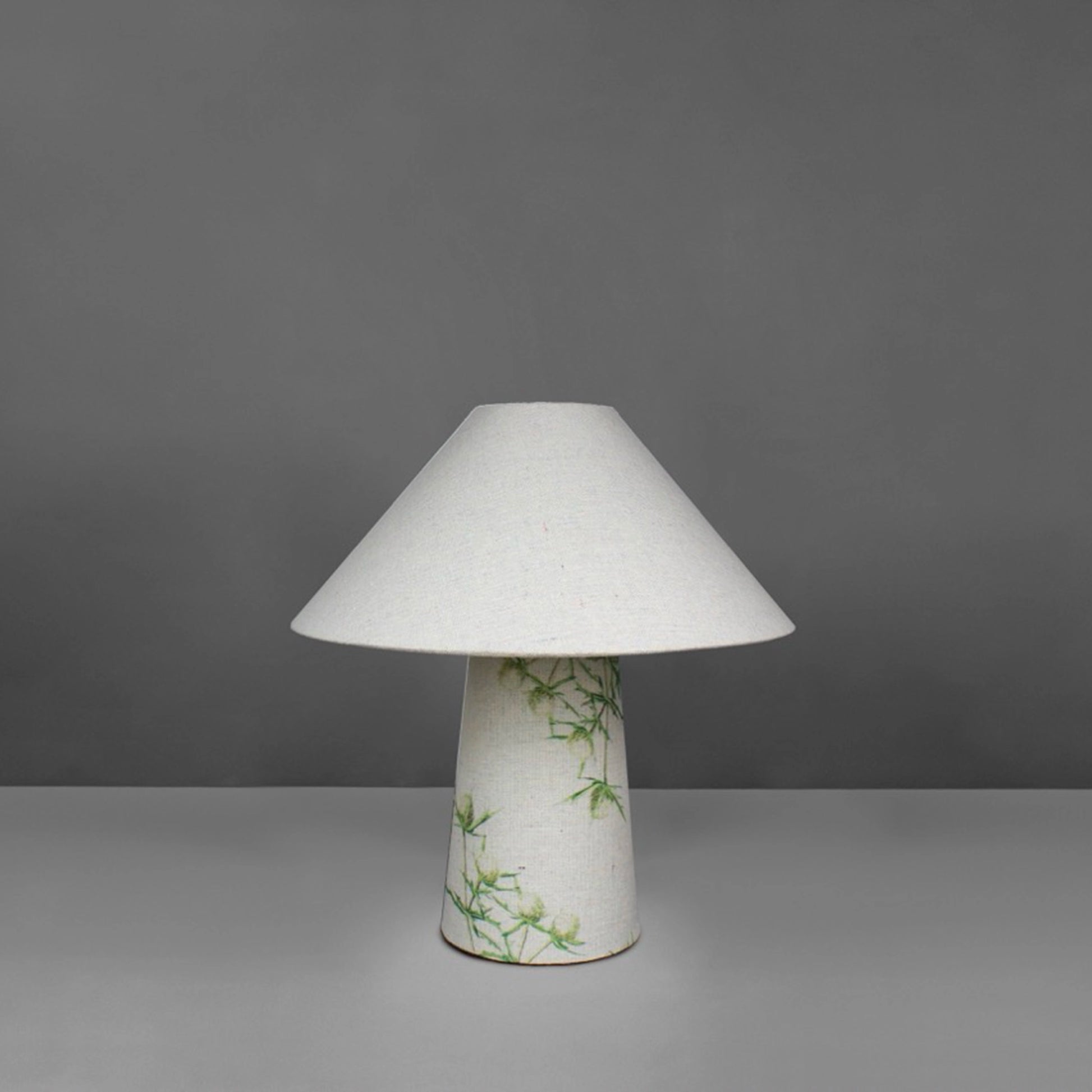 A small fabric table lamp with shade and a thistle design on the conical base