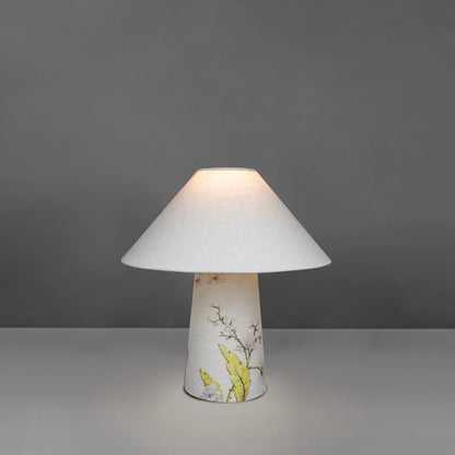 A small fabric table lamp with shade and a yellow blossom design on the conical base lit up