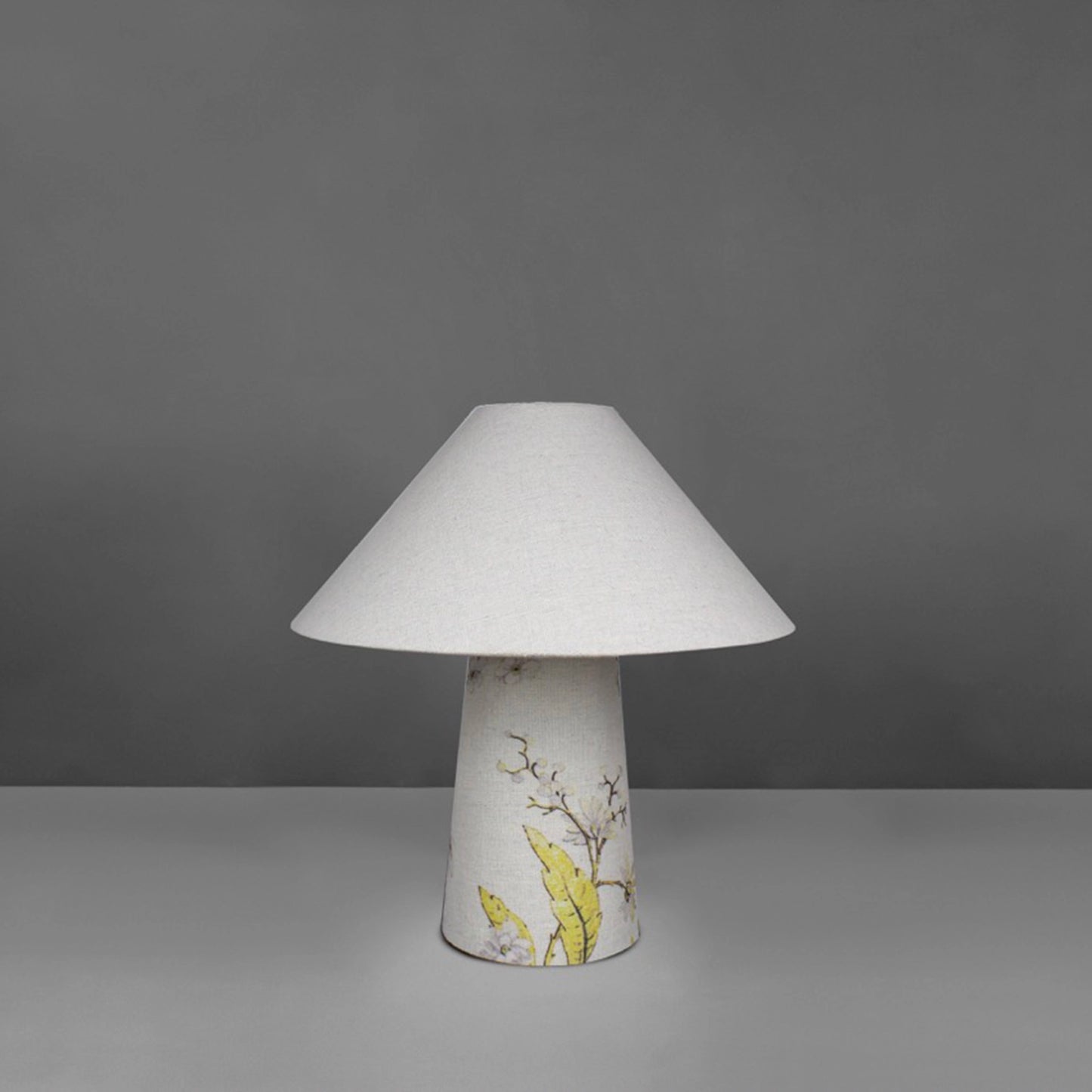 A small fabric table lamp with shade and a yellow blossom design on the conical base