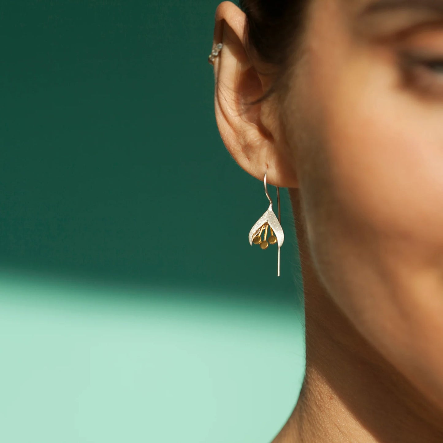 Model wearing satin silver snowdrop earrings with gold stamen details and long hooks