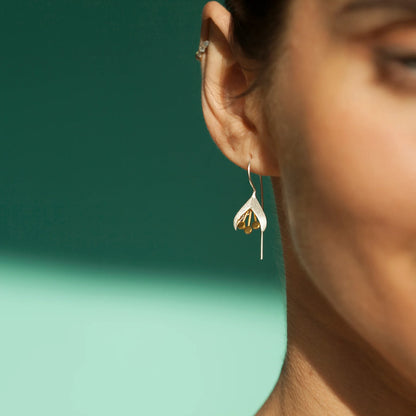 Model wearing satin silver snowdrop earrings with gold stamen details and long hooks
