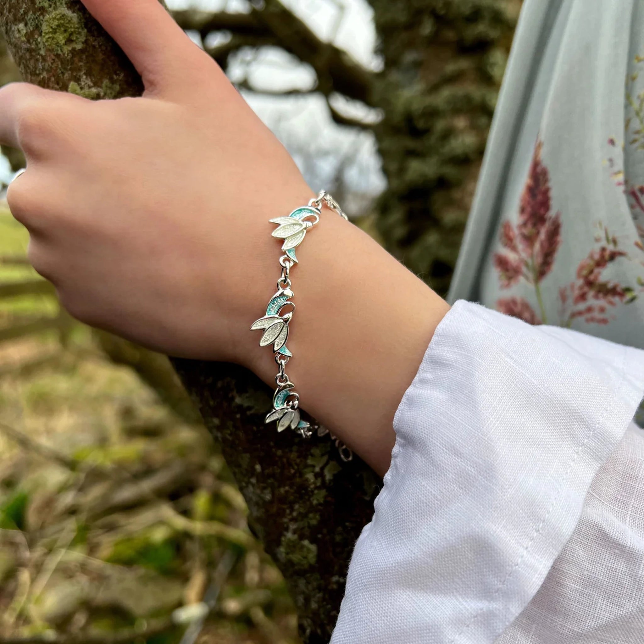 Model wearing silver bracelet with snowdrop flower links in a green and crystal white enamel 