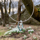 Silver necklet with four snowdrop flowers in an oval shape, with green and white enamel on a neck wire posed outside