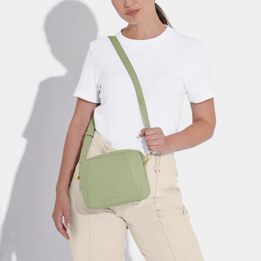 Model wearing soft sage crossbody bag in a simple box shape with adjustable strap and gold hardware